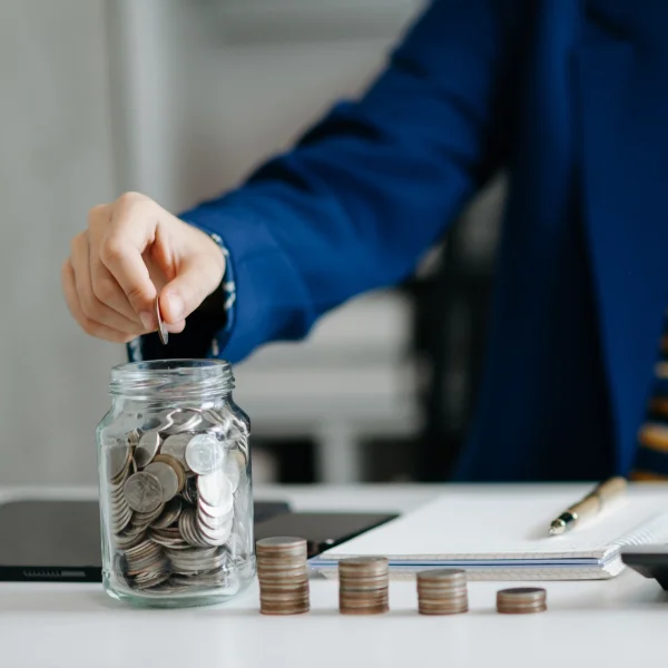 A woman carefully places coins into a jar, symbolizing her commitment to budgeting and saving money.