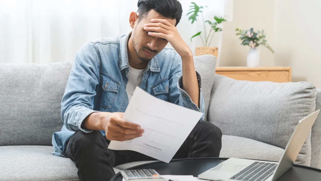 A man, sits on a couch with a laptop and papers, focused on his work.