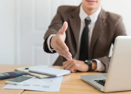 A man in a suit extends his hand for a handshake, symbolizing a professional greeting or agreement.