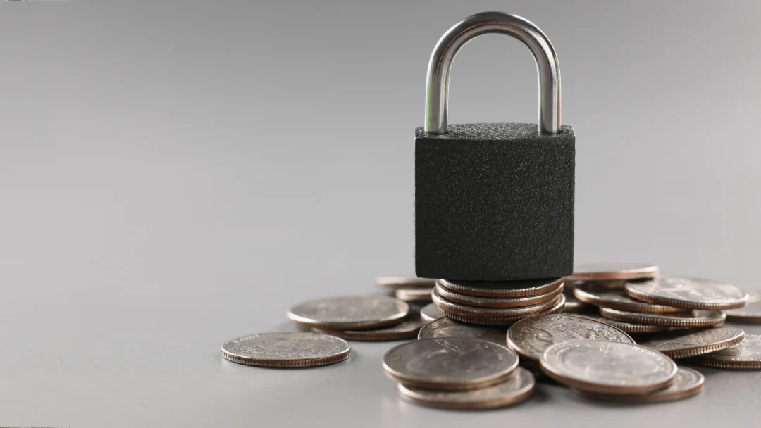 A padlock rests on a stack of coins, symbolizing financial security and protection of assets.