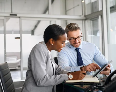 Two business professionals examining a tablet computer together, engaged in a discussion about their work.