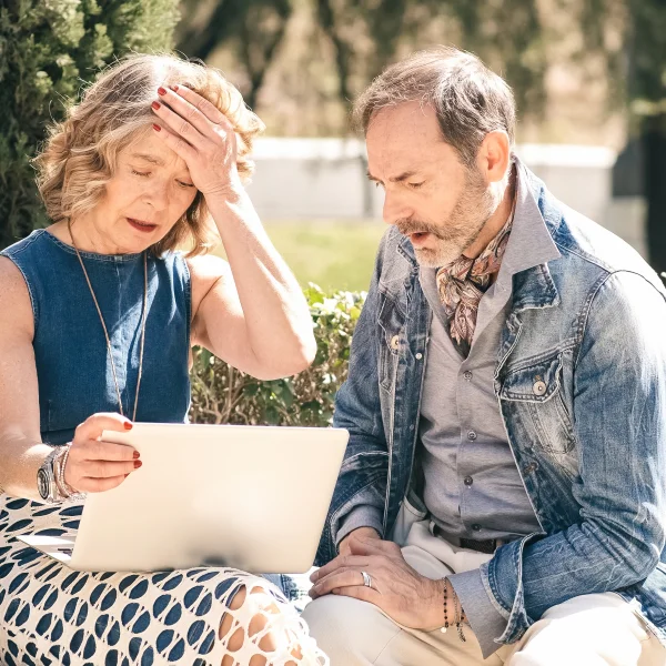 A man and woman on a bench, intently viewing a laptop, engaged in discussions about their financial security.