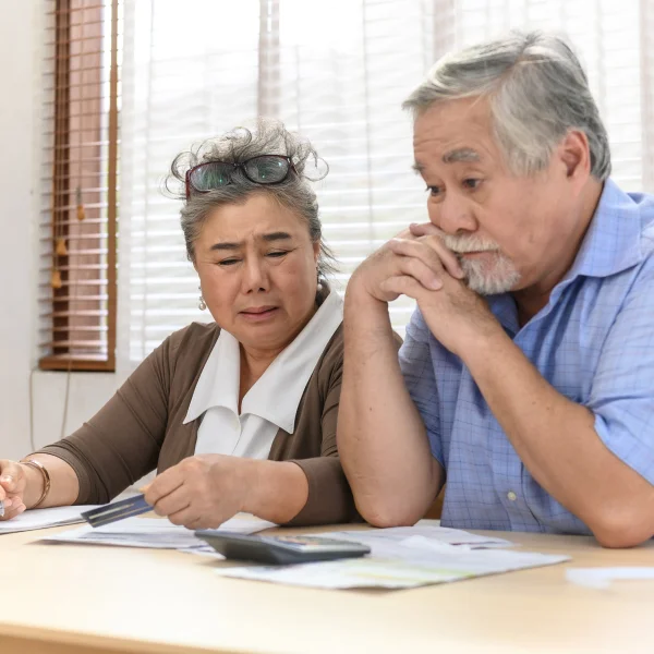 An elderly couple reviews financial paperwork together, discussing their financial situation with focused expressions.